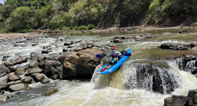 A person wearing safety gear paddles a watercraft over a small waterfall